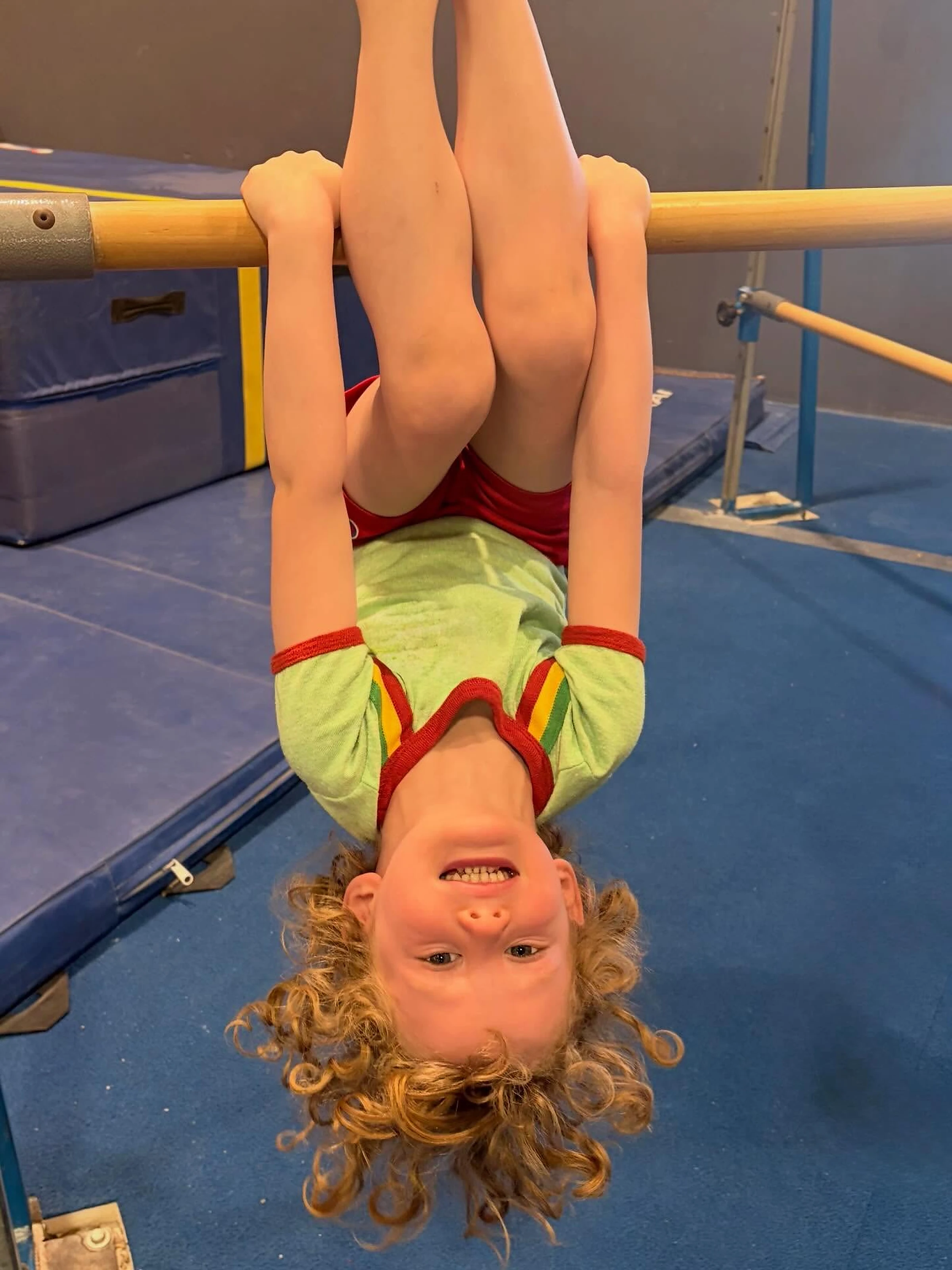 A young gymnast hanging upside down on the bars at Old Pueblo Gymnastics Academy