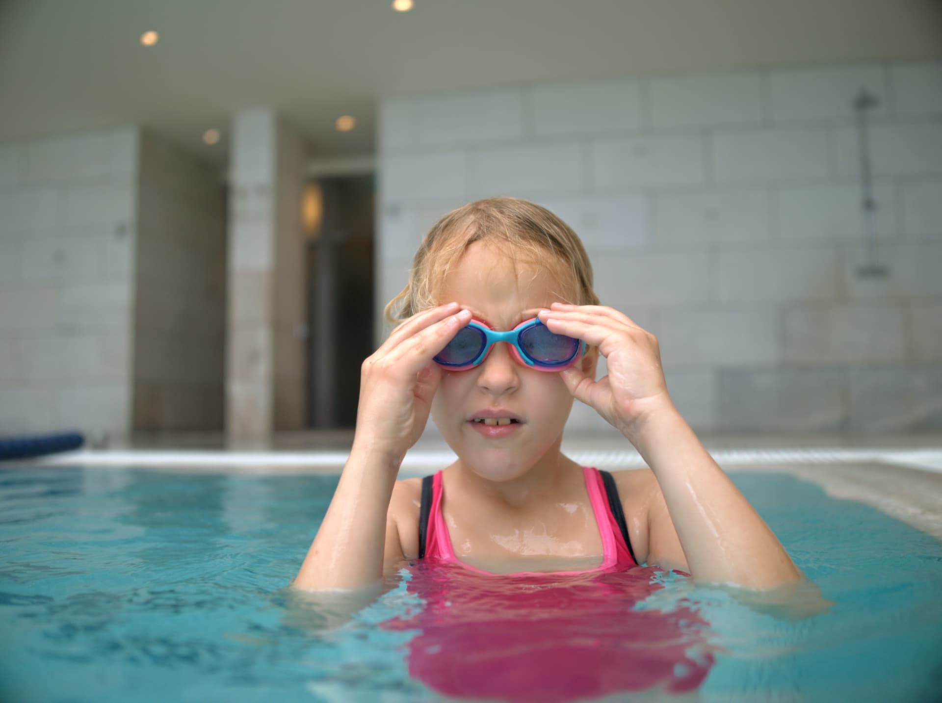 Child adjusting swim goggles in a pool